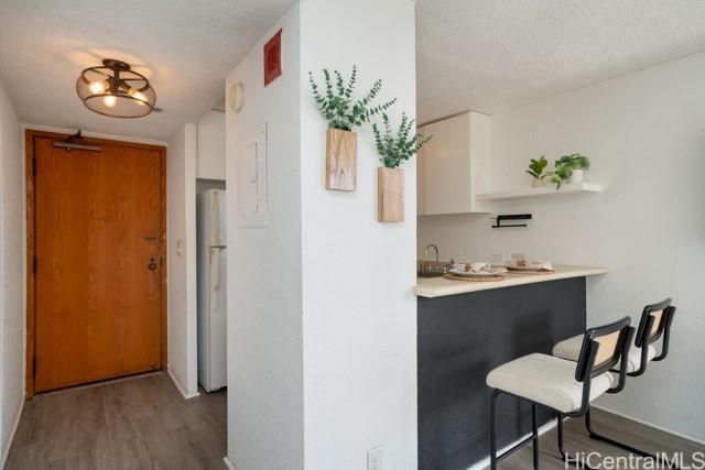 300 Wai Nani Way Unit 1815, Honolulu, HI 96815 - kitchen featuring freestanding refrigerator, wood finished floors, a breakfast bar, baseboards, and a textured ceiling
