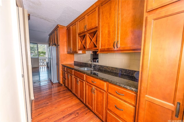 84-965 Farrington Hwy Unit B216, Waianae, HI 96792 - kitchen with a sink, light wood-style floors, a textured ceiling, brown cabinets, and dark stone counters
