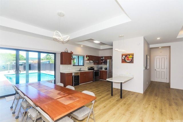 dining room with a raised ceiling, light wood-style floors, and recessed lighting