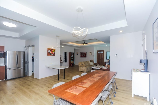 dining room featuring a raised ceiling, a barn door, and light wood finished floors