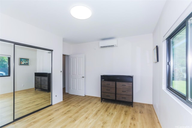 unfurnished bedroom featuring a wall unit AC, light wood-style floors, and a closet