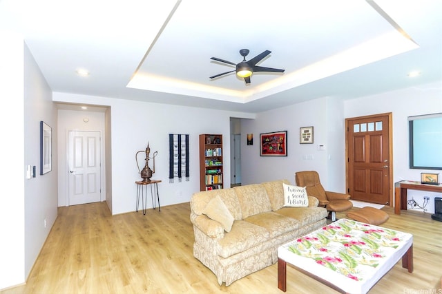 living area with a raised ceiling, light wood-style flooring, ceiling fan, and recessed lighting