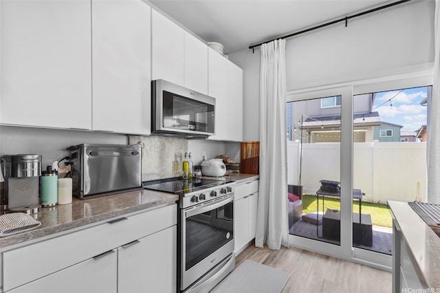 91-1640 Honouliuli St Unit 109, Ewa Beach, HI 96706 - kitchen with appliances with stainless steel finishes, white cabinetry, light wood-type flooring, light stone countertops, and backsplash