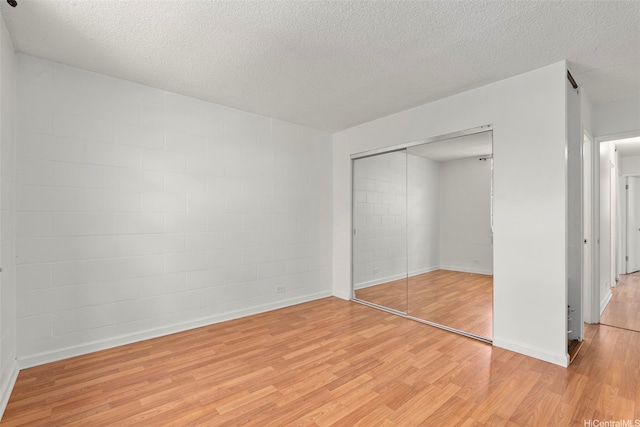 98-1042 Moanalua Rd Unit 2-303, Aiea, HI 96701 - unfurnished bedroom with light wood-type flooring, concrete block wall, a closet, and a textured ceiling