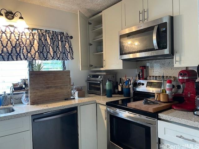 47-166 Wailehua Rd, Kaneohe, HI 96744 - kitchen featuring appliances with stainless steel finishes, plenty of natural light, white cabinetry, a textured ceiling, and light stone counters