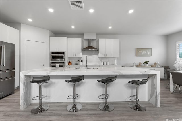 91-1669 Mee St, Ewa Beach, HI 96706 - kitchen featuring appliances with stainless steel finishes, wall chimney exhaust hood, a breakfast bar area, white cabinetry, and a large island with sink