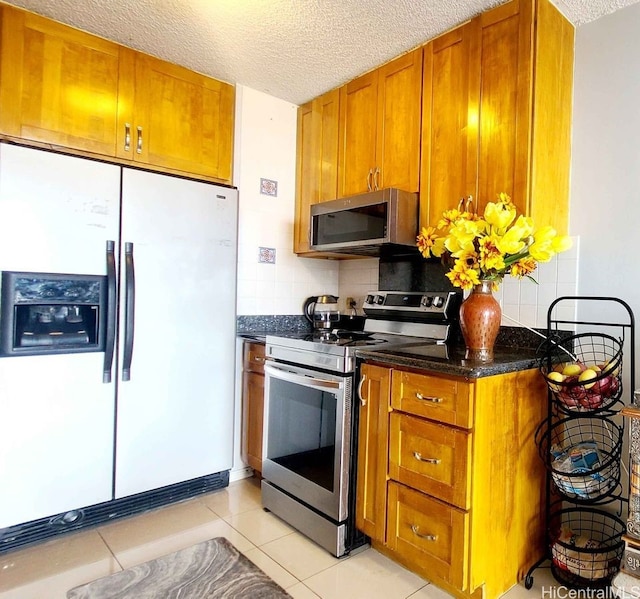 3161 Ala Ilima St Unit 2112, Honolulu, HI 96818 - kitchen with stainless steel appliances, brown cabinets, a textured ceiling, dark stone counters, and decorative backsplash