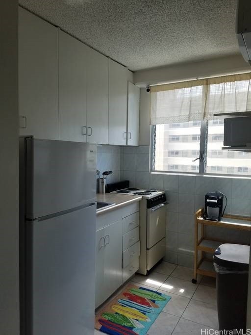 747 Amana St Unit 1515, Honolulu, HI 96814 - kitchen featuring freestanding refrigerator, white electric range, white cabinets, light tile patterned flooring, and a textured ceiling