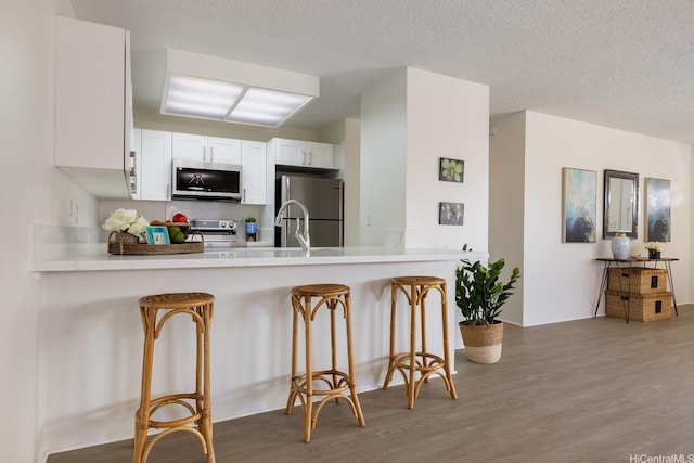 94-1444 Okupu St, Waipahu, HI 96797 - kitchen with stainless steel appliances, a peninsula, wood finished floors, a breakfast bar, and light countertops