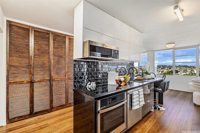 2825 S King St Unit 1403, Honolulu, HI 96826 - kitchen with stainless steel appliances, white cabinetry, light wood-style floors, a sink, and dark countertops