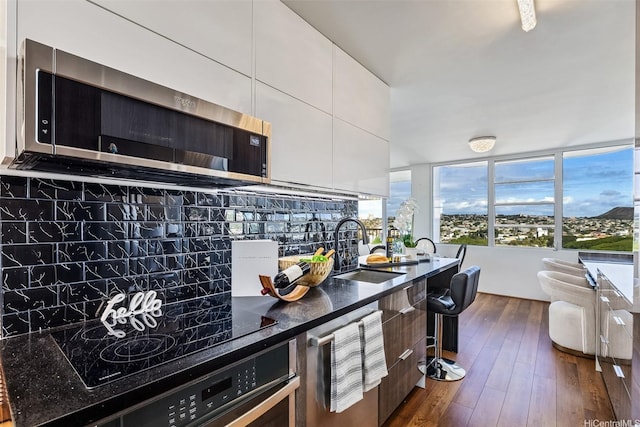2825 S King St Unit 1403, Honolulu, HI 96826 - kitchen with a sink, white cabinetry, dark wood finished floors, stainless steel microwave, and tasteful backsplash