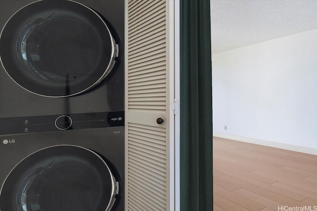 990 Ala Nanala St Unit 27D, Honolulu, HI 96818 - laundry room featuring stacked washing machine and dryer, wood finished floors, baseboards, and a textured ceiling