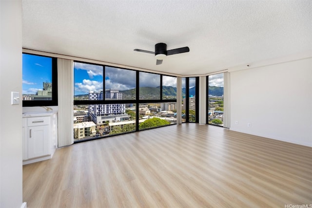 2724 Kahoaloha Ln Unit 1407, Honolulu, HI 96826 - unfurnished living room with a wall of windows, a textured ceiling, a ceiling fan, light wood finished floors, and a city view