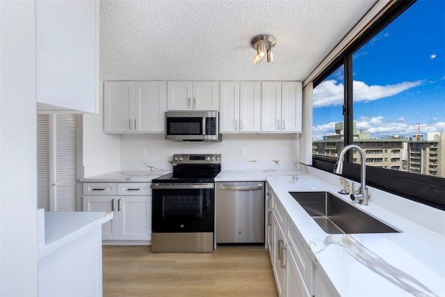 2724 Kahoaloha Ln Unit 1407, Honolulu, HI 96826 - kitchen featuring stainless steel appliances, a sink, a textured ceiling, white cabinets, and light wood-style flooring