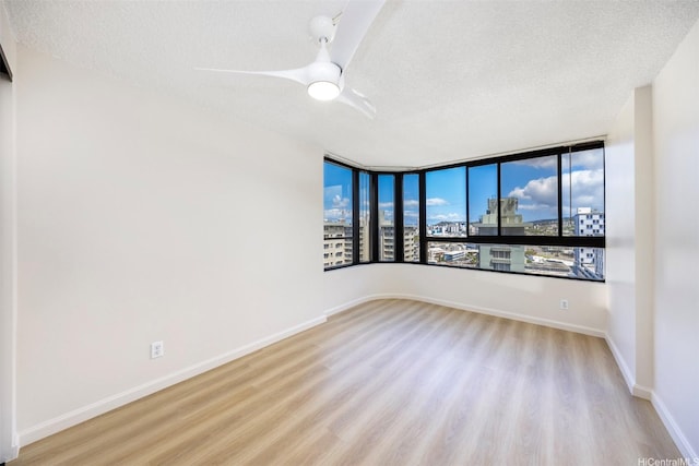 2724 Kahoaloha Ln Unit 1407, Honolulu, HI 96826 - empty room featuring a textured ceiling, wood finished floors, a city view, a ceiling fan, and baseboards