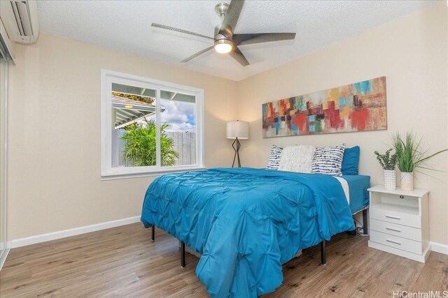 94-457 Akoa Pl, Mililani, HI 96789 - bedroom featuring wood finished floors, baseboards, a wall mounted AC, a textured ceiling, and a ceiling fan
