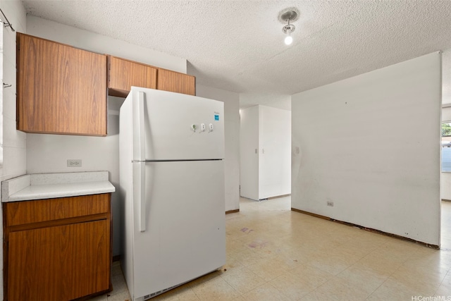 94-533 Ulieo St, Waipahu, HI 96797 - kitchen featuring freestanding refrigerator, a textured ceiling, brown cabinets, light flooring, and light countertops