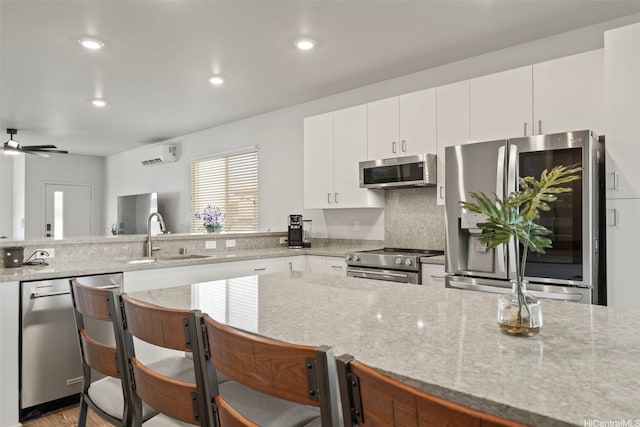 91-1774 Kohanahana Loop, Ewa Beach, HI 96706 - kitchen featuring appliances with stainless steel finishes, light stone counters, a wall mounted air conditioner, white cabinets, and a breakfast bar area