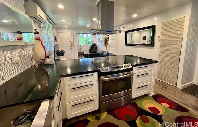 91-1708 Bond St, Ewa Beach, HI 96706 - kitchen featuring stainless steel electric range oven, island range hood, white cabinetry, a wall mounted air conditioner, and dark countertops