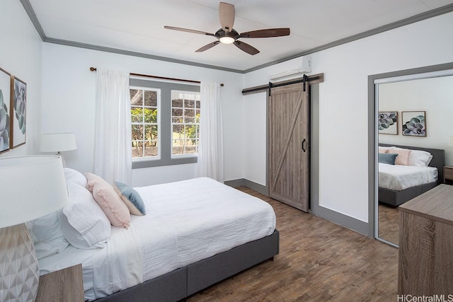 bedroom with a barn door, ornamental molding, a wall mounted AC, wood finished floors, and a ceiling fan