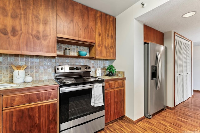 1525 Wilder Ave Unit 903, Honolulu, HI 96822 - kitchen featuring stainless steel appliances, tile countertops, light wood-style flooring, backsplash, and baseboards