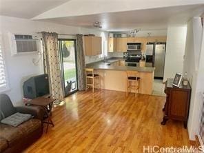 95-233 Halepule Pl Unit 44, Honolulu, HI 96789 - kitchen with appliances with stainless steel finishes, a peninsula, a wall mounted AC, light wood-type flooring, and a kitchen bar