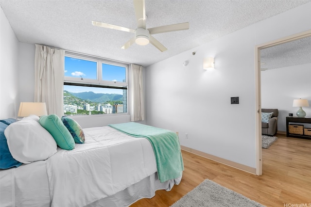 1450 Young St Unit 2004, Honolulu, HI 96814 - bedroom with a textured ceiling, light wood-style flooring, a ceiling fan, a mountain view, and baseboards