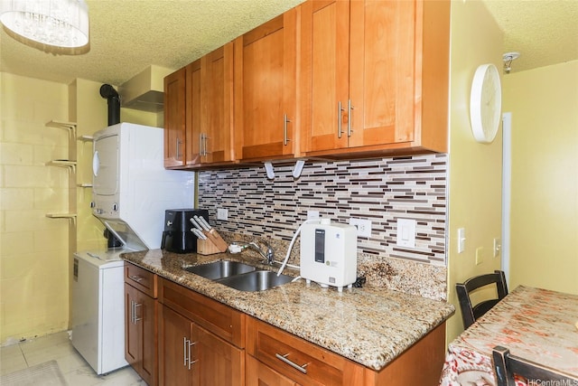 1260 Richard Ln Unit B601, Honolulu, HI 96819 - kitchen featuring stacked washer and clothes dryer, a textured ceiling, tasteful backsplash, brown cabinets, and light stone countertops