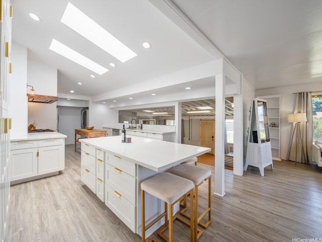67-342 Kukea Cir, Waialua, HI 96791 - kitchen with a sink, a kitchen bar, white cabinets, a skylight, and light wood-type flooring