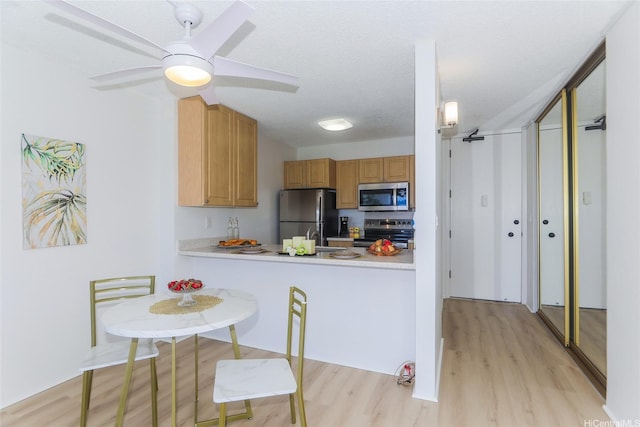 98-500 Koauka Loop Unit 23H, Aiea, HI 96701 - kitchen featuring appliances with stainless steel finishes, light wood-style floors, light countertops, a ceiling fan, and a peninsula
