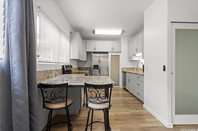 1447 Kewalo St Unit 101, Honolulu, HI 96822 - kitchen with appliances with stainless steel finishes, a sink, a breakfast bar, a peninsula, and light stone countertops