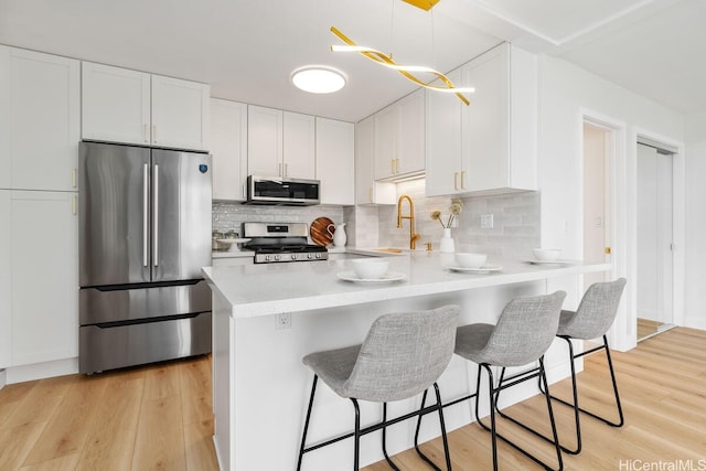 53-549 Kamehameha Hwy Unit 402, Hauula, HI 96717 - kitchen with appliances with stainless steel finishes, light countertops, a breakfast bar area, white cabinets, and light wood-type flooring