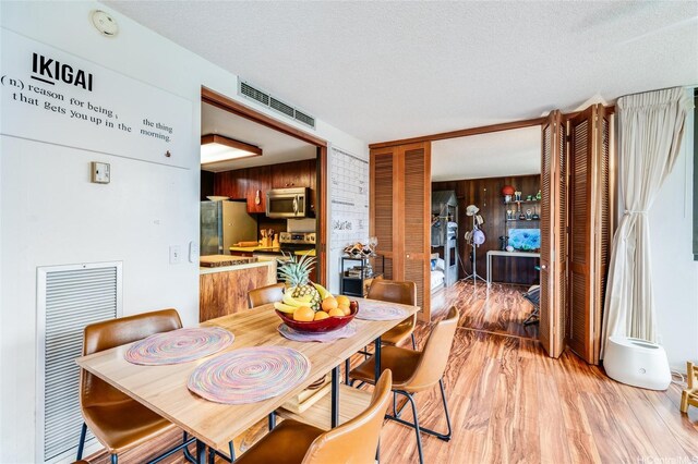 250 Kawaihae St Unit 10E, Honolulu, HI 96825 - dining space with a textured ceiling, light wood-type flooring, and wood walls