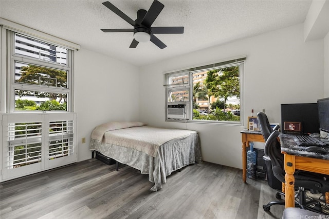 3009 Ala Makahala Pl Unit 214, Honolulu, HI 96818 - bedroom with multiple windows, a desk, wood finished floors, a textured ceiling, and ceiling fan