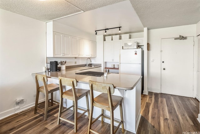 3045 Ala Napuaa Pl Unit 1803, Honolulu, HI 96818 - kitchen with a peninsula, dark wood-style flooring, freestanding refrigerator, a breakfast bar area, and white cabinets