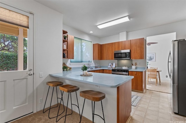 91-1032 Kauoha St, Ewa Beach, HI 96706 - kitchen featuring stainless steel appliances, brown cabinets, a peninsula, light floors, and a kitchen bar