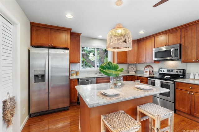 66-912 Kamakahala St Unit 2, Waialua, HI 96791 - kitchen featuring stainless steel appliances, light wood-type flooring, brown cabinetry, light stone countertops, and a kitchen island