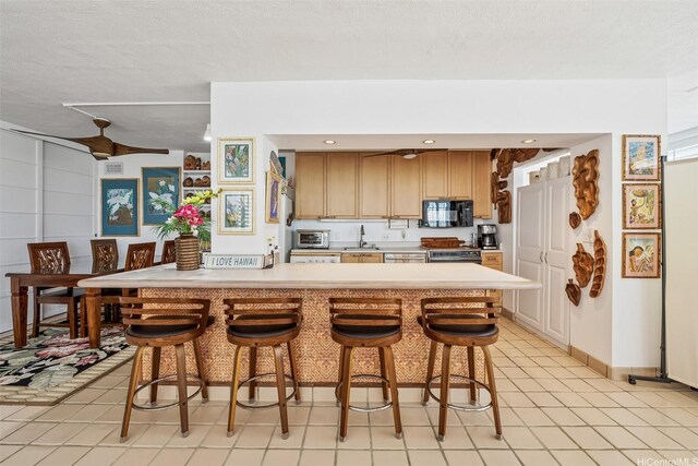 2801 Coconut Ave Unit 2D, Honolulu, HI 96815 - kitchen featuring black microwave, a breakfast bar area, light countertops, stove, and light tile patterned floors