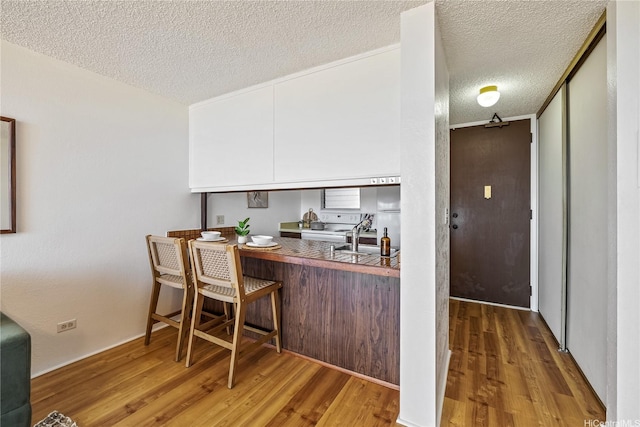 98-099 Uao Pl Unit 506, Aiea, HI 96701 - kitchen with wood finished floors, a textured ceiling, white electric range oven, and a breakfast bar