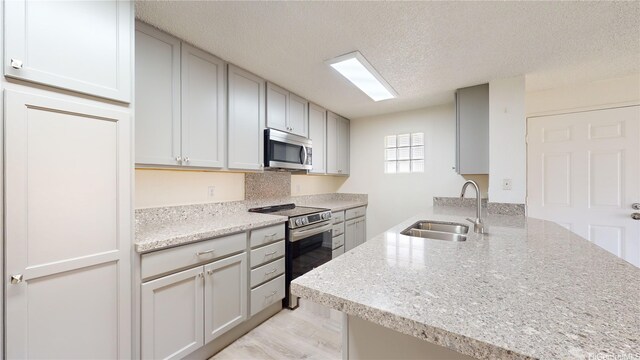 91-1201 Kaneana St Unit 3J, Ewa Beach, HI 96706 - kitchen with appliances with stainless steel finishes, a peninsula, a textured ceiling, light stone counters, and gray cabinets