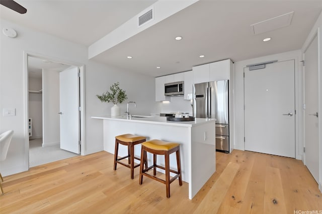 1001 Queen St Unit 2506, Honolulu, HI 96814 - kitchen featuring appliances with stainless steel finishes, light wood finished floors, white cabinetry, a peninsula, and a kitchen bar