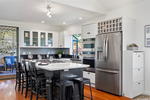 2633B Nahaku Pl Unit H, Honolulu, HI 96826 - kitchen featuring stainless steel appliances, wood finished floors, white cabinetry, a breakfast bar area, and glass insert cabinets
