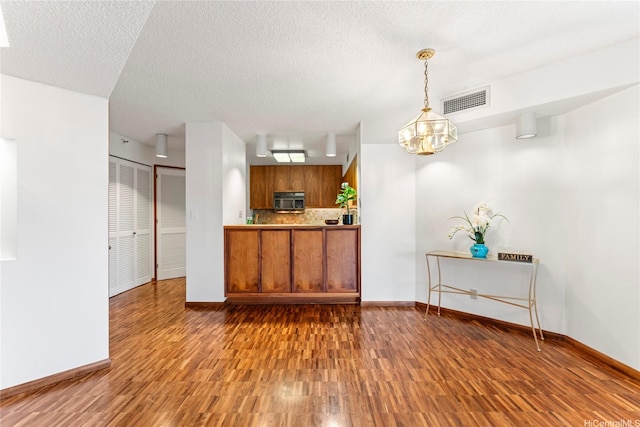 1525 Wilder Ave Unit 401, Honolulu, HI 96822 - kitchen featuring stainless steel microwave, brown cabinetry, wood finished floors, decorative backsplash, and a textured ceiling
