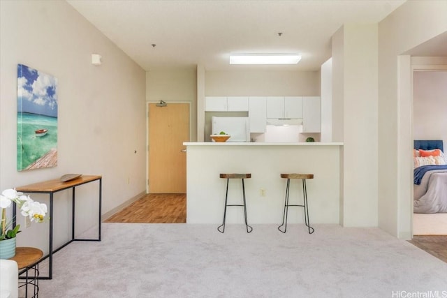 3009 Ala Makahala Pl Unit 102, Honolulu, HI 96818 - kitchen featuring refrigerator, light carpet, white cabinetry, a breakfast bar, and a peninsula