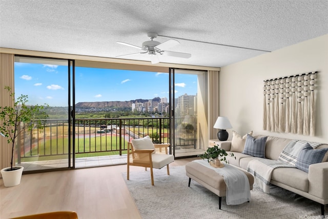 2444 Hihiwai St Unit 902, Honolulu, HI 96826 - living area featuring wood finished floors, expansive windows, a ceiling fan, a textured ceiling, and a mountain view