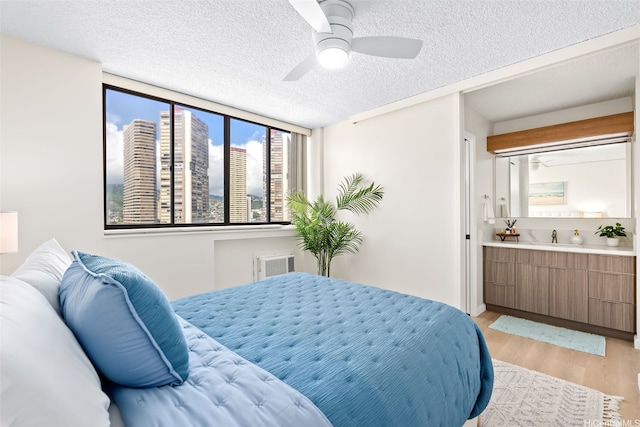 2444 Hihiwai St Unit 902, Honolulu, HI 96826 - bedroom featuring light wood-type flooring, a textured ceiling, ensuite bathroom, a ceiling fan, and a wall mounted air conditioner