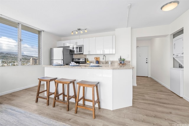 2345 Ala Wai Blvd Unit 1918, Honolulu, HI 96815 - kitchen featuring stainless steel appliances, stacked washer and clothes dryer, a breakfast bar area, light wood-type flooring, and white cabinetry