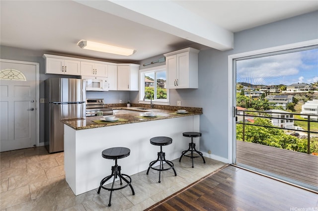 1048 Kaupaku Pl, Honolulu, HI 96825 - kitchen with stainless steel appliances, a peninsula, white cabinetry, dark stone counters, and a kitchen bar