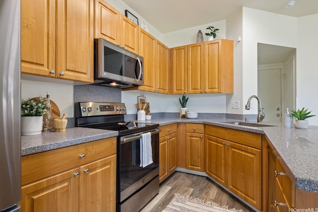 91-1221 Kanela St Unit M54, Ewa Beach, HI 96706 - kitchen with appliances with stainless steel finishes, light wood-type flooring, dark stone countertops, a peninsula, and brown cabinets