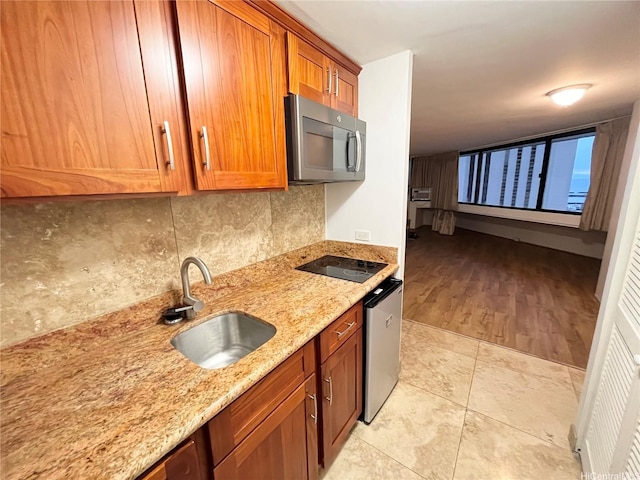 1700 Ala Moana Blvd Unit 1702, Honolulu, HI 96815 - kitchen with stainless steel microwave, black electric cooktop, decorative backsplash, light stone countertops, and brown cabinetry
